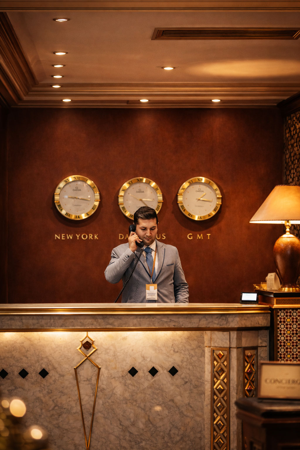 Receptionist at Damarose Hotel front desk with world timezone clocks